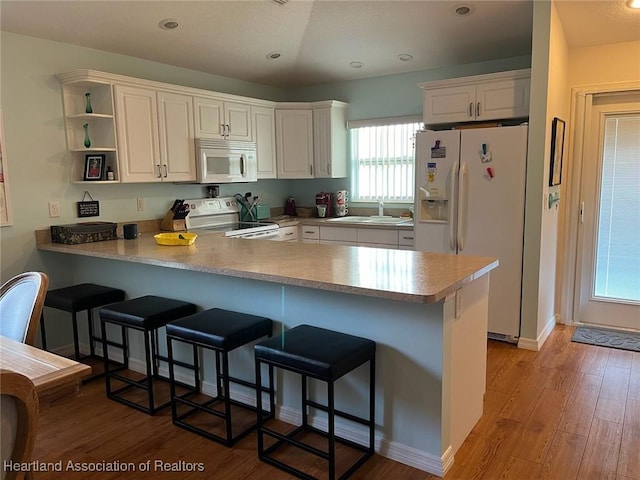 kitchen with kitchen peninsula, white appliances, a breakfast bar, white cabinets, and light wood-type flooring