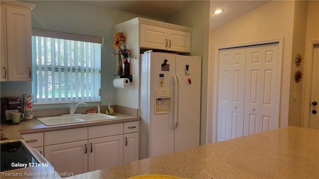 kitchen featuring lofted ceiling, white cabinetry, sink, and white refrigerator with ice dispenser