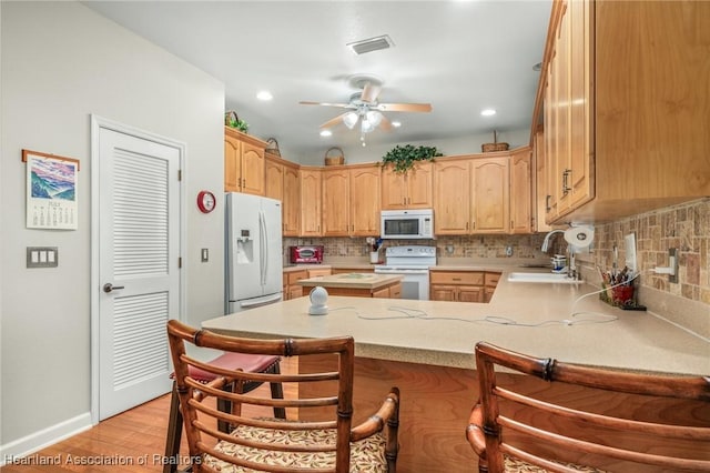 kitchen with kitchen peninsula, a kitchen bar, white appliances, and sink