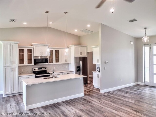 kitchen with a kitchen island with sink, white cabinets, hanging light fixtures, decorative backsplash, and appliances with stainless steel finishes