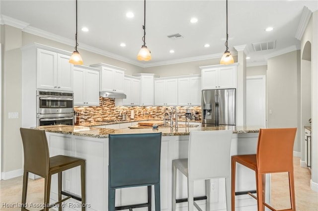 kitchen featuring a large island, stainless steel appliances, decorative light fixtures, white cabinets, and a breakfast bar