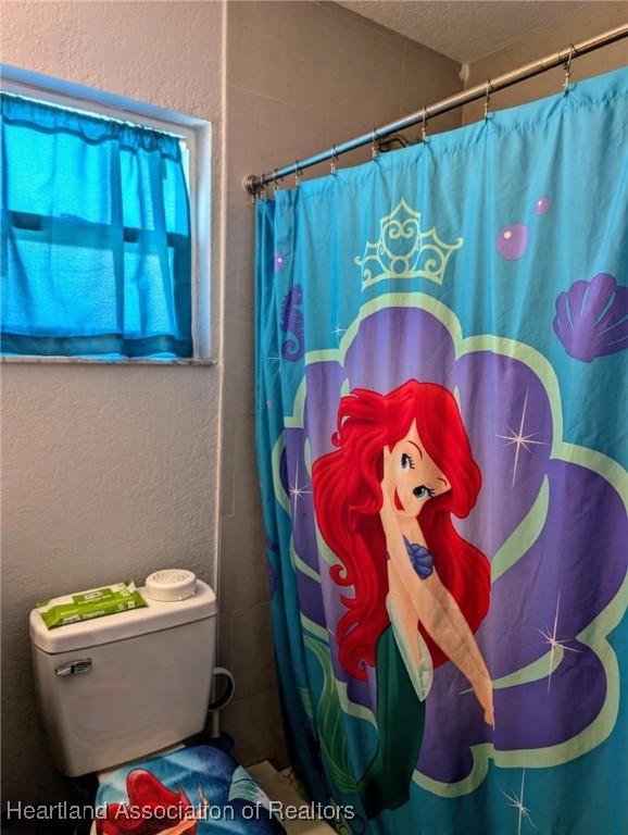4128 Capri St, Sebring, FL 33872 - bathroom featuring toilet, a textured wall, and a shower with shower curtain