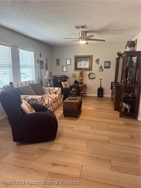4128 Capri St, Sebring, FL 33872 - living room with light wood-style floors, a textured ceiling, a ceiling fan, baseboards, and visible vents