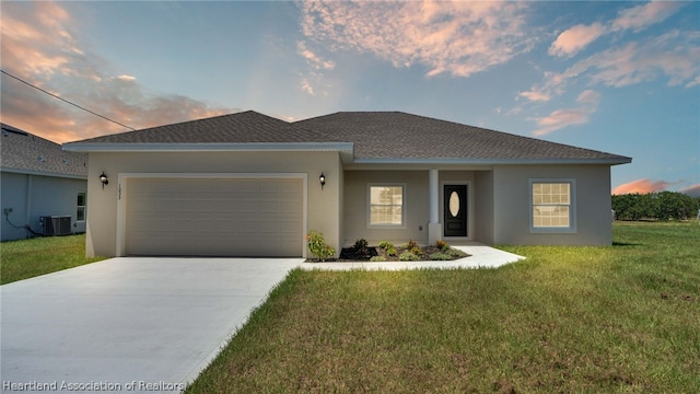 view of front of home with central air condition unit, a garage, and a lawn