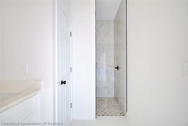 bathroom featuring tile patterned flooring, a tile shower, and vanity