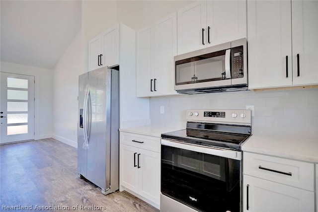 kitchen with vaulted ceiling, white cabinetry, stainless steel appliances, and light hardwood / wood-style flooring