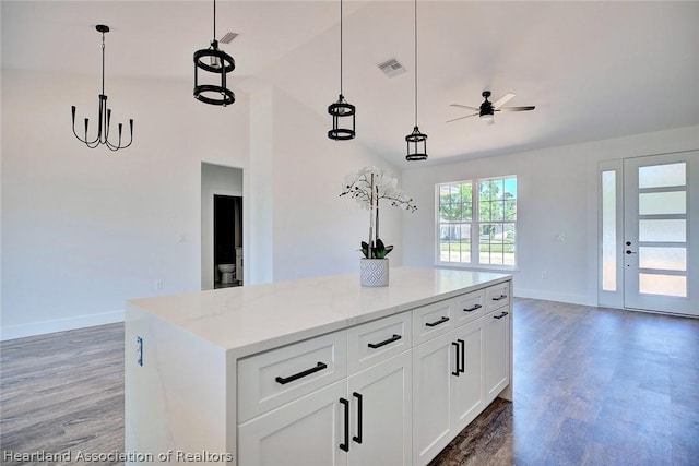 kitchen featuring light stone countertops, white cabinetry, hanging light fixtures, a kitchen island, and ceiling fan with notable chandelier