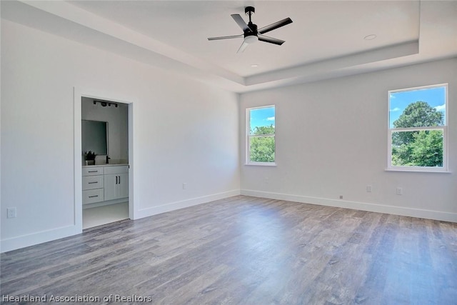 empty room with hardwood / wood-style flooring, a raised ceiling, and ceiling fan