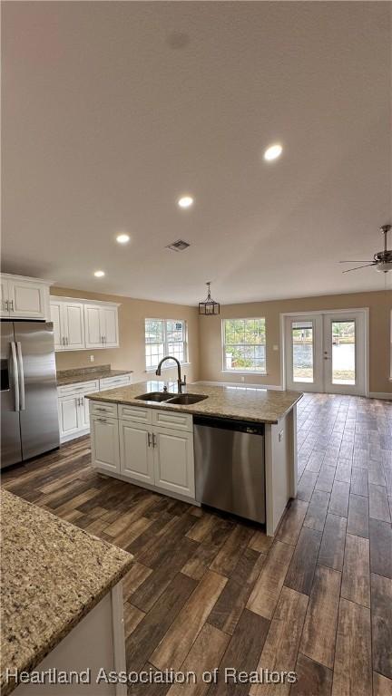 kitchen featuring light stone counters, stainless steel appliances, sink, a center island with sink, and white cabinets