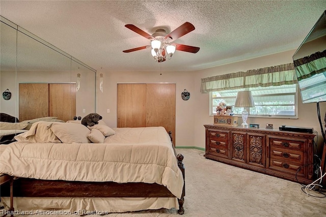 carpeted bedroom featuring a textured ceiling, two closets, and ceiling fan