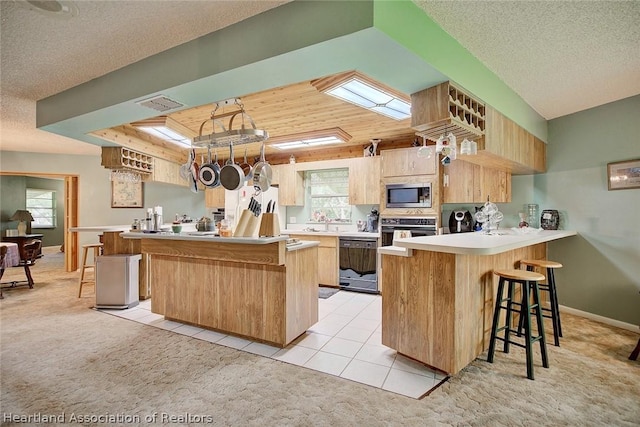 kitchen featuring kitchen peninsula, black appliances, light colored carpet, and a kitchen breakfast bar