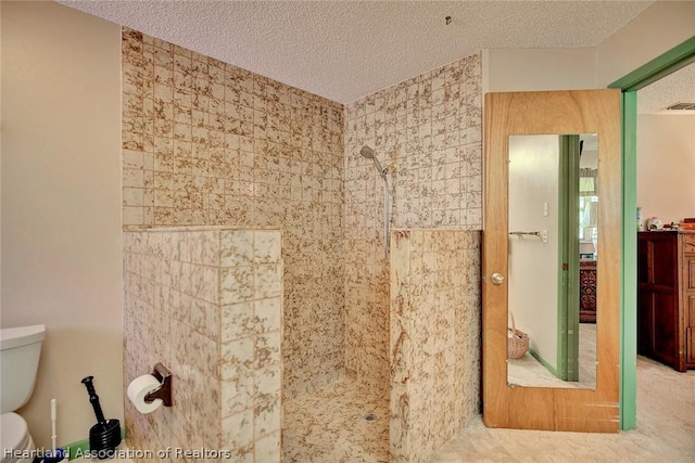 bathroom featuring toilet, tiled shower, and a textured ceiling