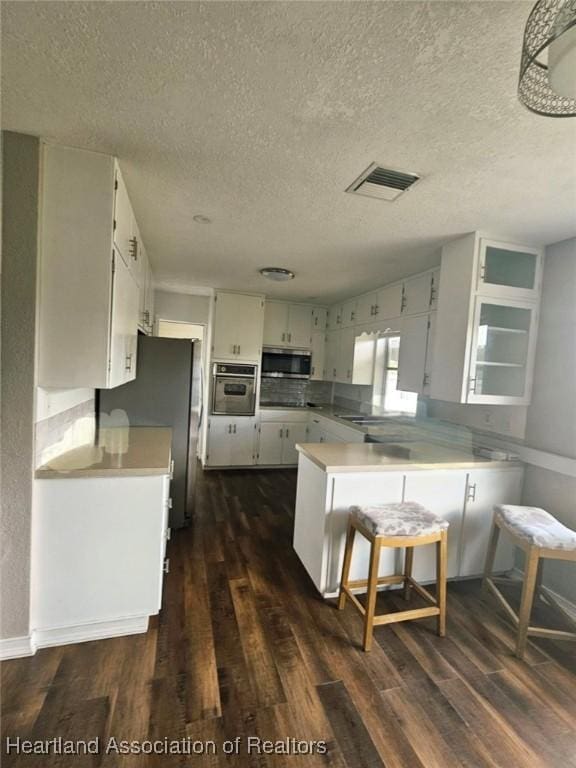 908 Taseschee Dr, Sebring, FL 33870 - kitchen with appliances with stainless steel finishes, a peninsula, dark wood finished floors, a textured ceiling, and light countertops