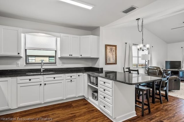 kitchen featuring white cabinets, a peninsula, a sink, vaulted ceiling, and visible vents