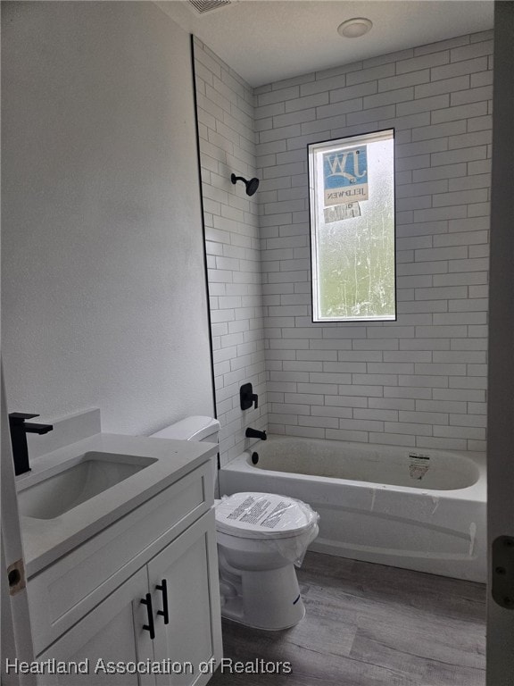 full bathroom featuring hardwood / wood-style flooring, tiled shower / bath combo, toilet, and vanity