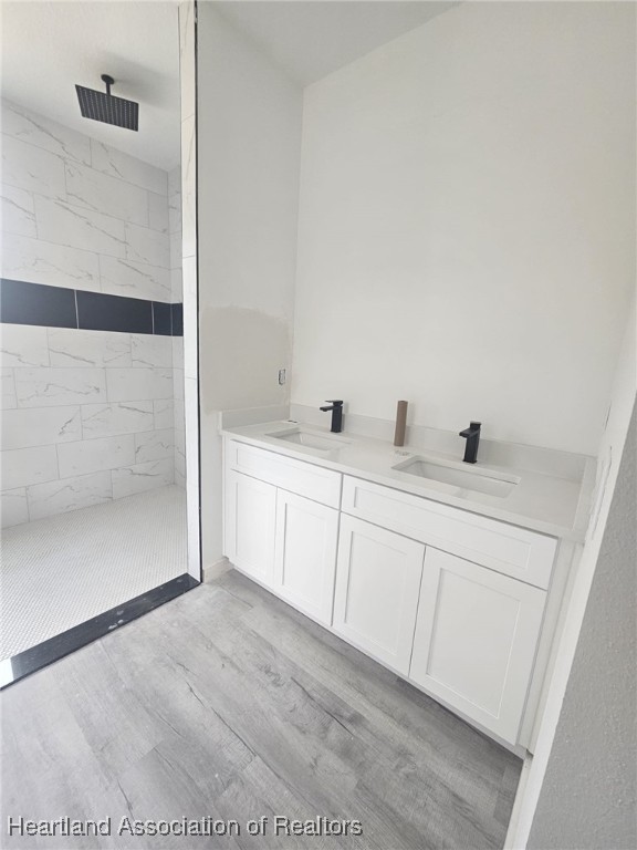 bathroom with a tile shower, vanity, and wood-type flooring