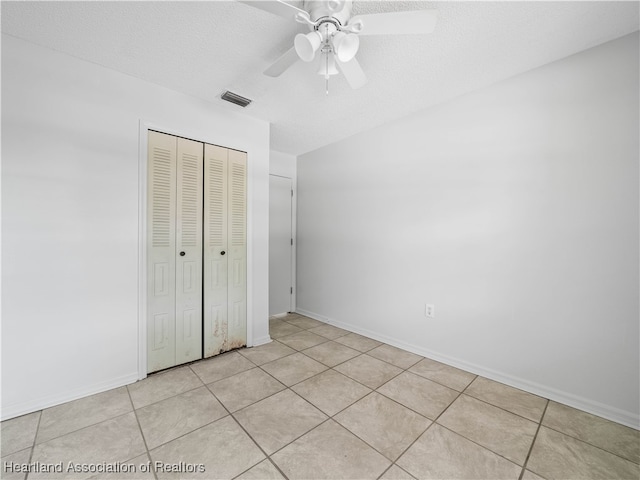 unfurnished bedroom featuring ceiling fan, a closet, light tile patterned floors, and a textured ceiling