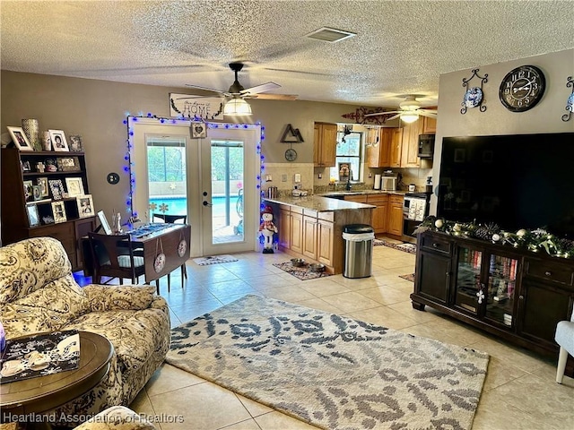 tiled living room featuring ceiling fan, french doors, and a textured ceiling