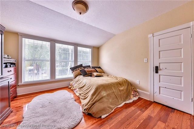 bedroom with a textured ceiling, multiple windows, light hardwood / wood-style flooring, and vaulted ceiling