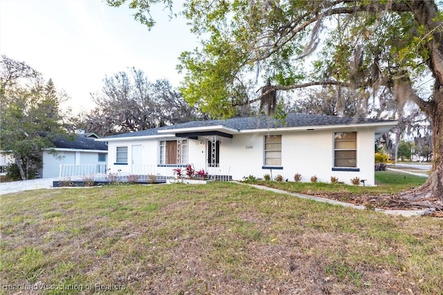 ranch-style home featuring covered porch, a front lawn, a shingled roof, and stucco siding