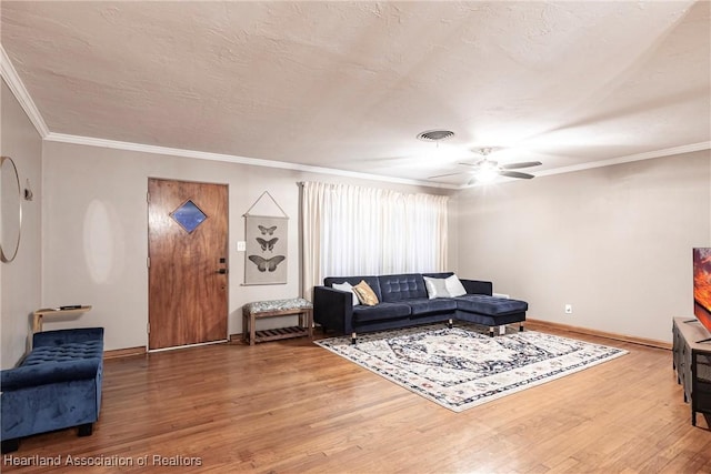 living room featuring visible vents, ornamental molding, a textured ceiling, wood finished floors, and baseboards