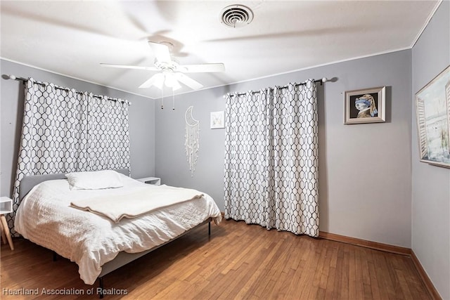 bedroom with visible vents, baseboards, a ceiling fan, wood-type flooring, and ornamental molding