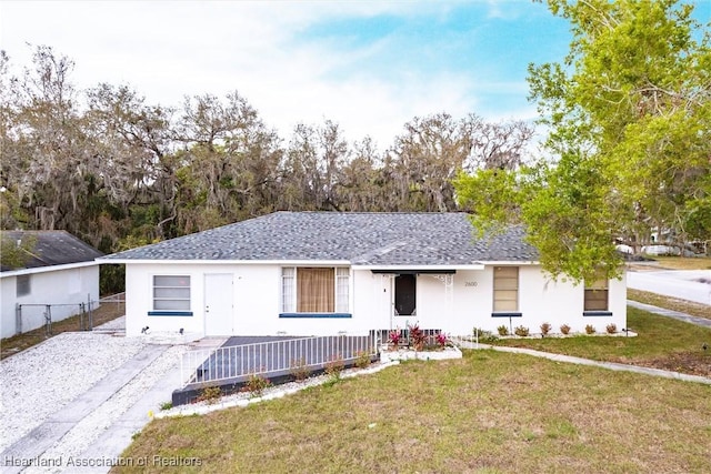 ranch-style house featuring a shingled roof, fence, a front lawn, and stucco siding