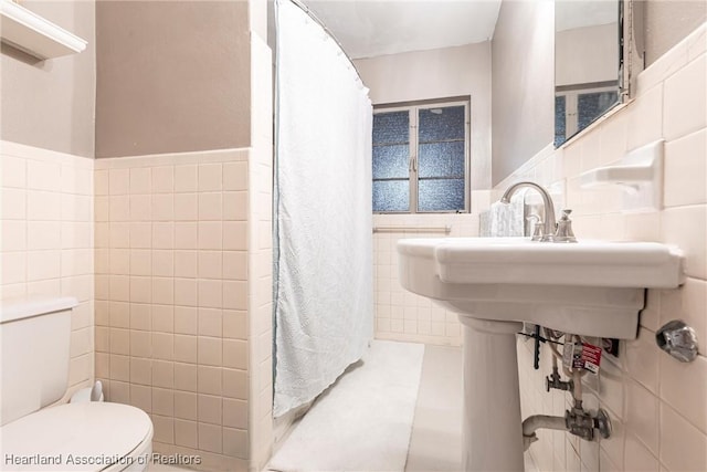 bathroom featuring toilet, curtained shower, and tile walls