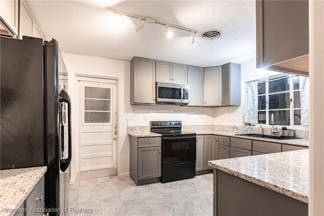 kitchen with light stone countertops, marble finish floor, gray cabinets, black appliances, and a sink