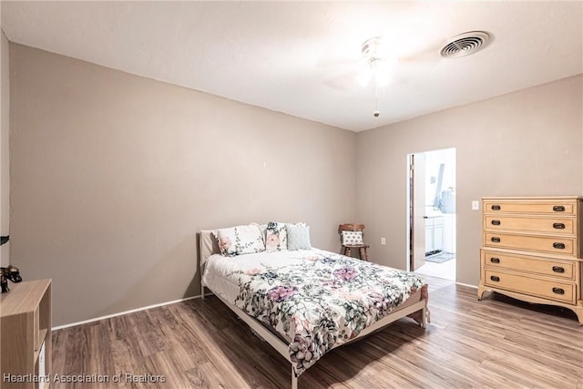 bedroom featuring ensuite bath, light wood-style flooring, visible vents, and baseboards