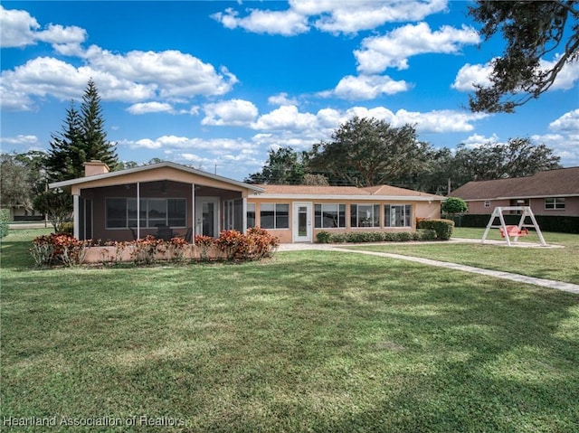 ranch-style home featuring a playground, a front lawn, and a sunroom