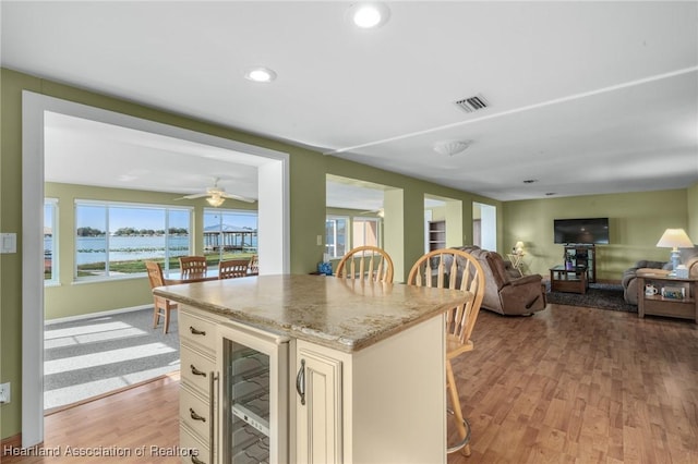 kitchen featuring light hardwood / wood-style flooring, a kitchen breakfast bar, beverage cooler, and light stone countertops