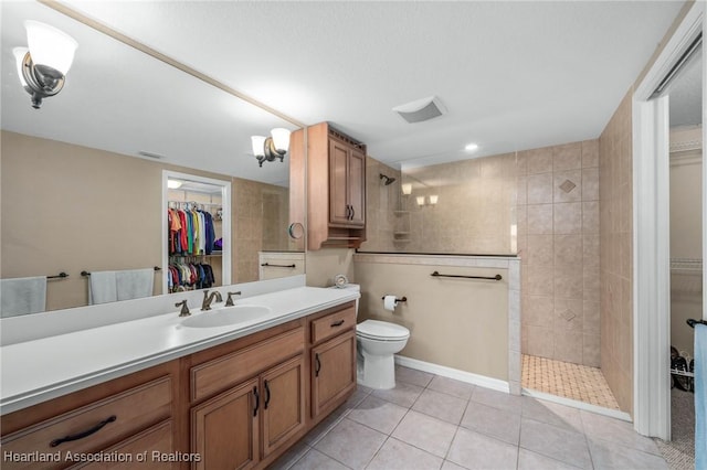 bathroom featuring toilet, tile patterned flooring, tiled shower, and vanity