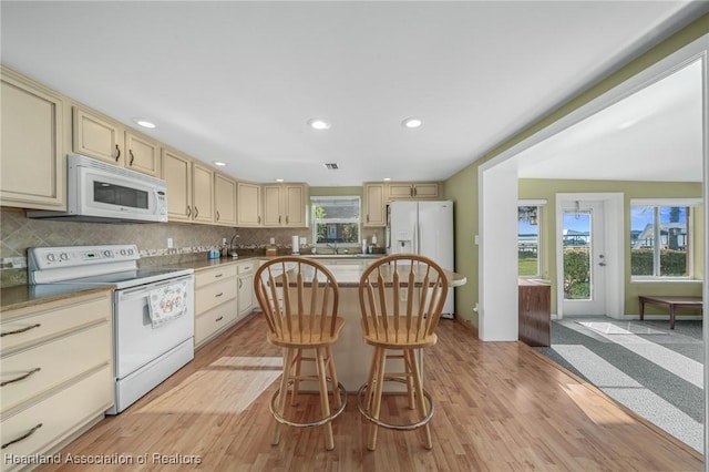 kitchen featuring cream cabinetry, white appliances, a kitchen breakfast bar, a wealth of natural light, and backsplash