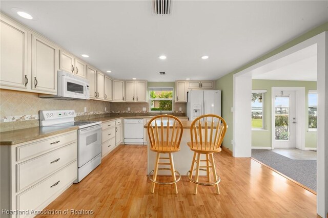 kitchen featuring white appliances, a kitchen breakfast bar, backsplash, light wood-type flooring, and recessed lighting
