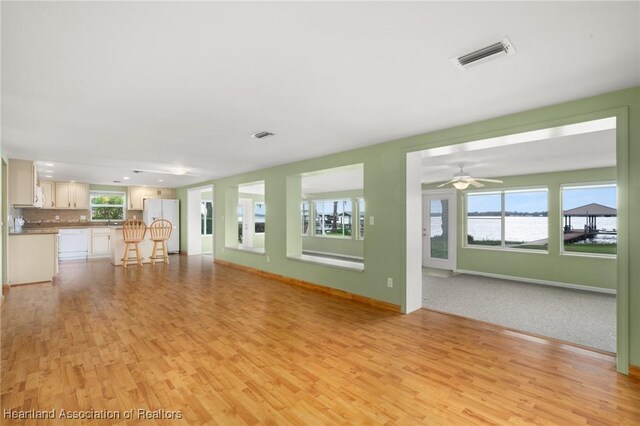 unfurnished living room featuring light wood-type flooring, baseboards, a water view, ceiling fan, and recessed lighting