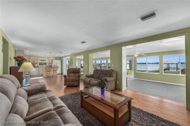 living room with light hardwood / wood-style floors, ceiling fan, a water view, and a textured ceiling