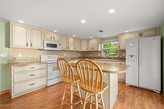 kitchen featuring white appliances, cream cabinetry, decorative backsplash, a kitchen island, and recessed lighting