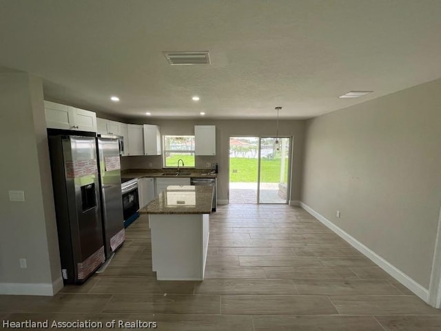 kitchen featuring stainless steel appliances, a kitchen island, sink, decorative light fixtures, and white cabinetry