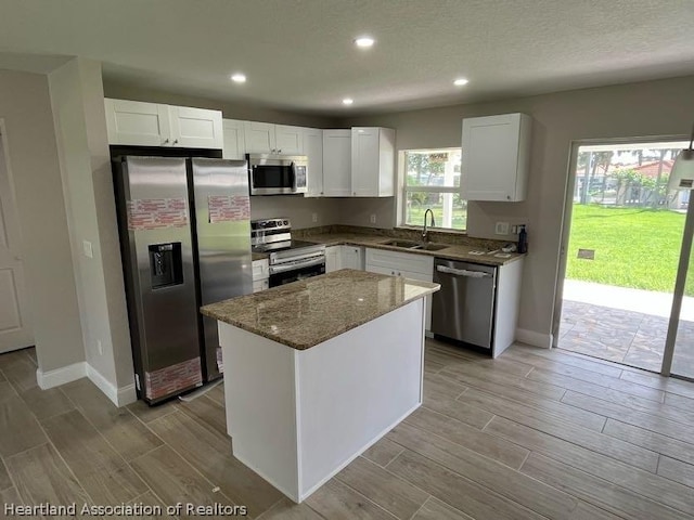 kitchen featuring stainless steel appliances, sink, stone counters, white cabinets, and a center island