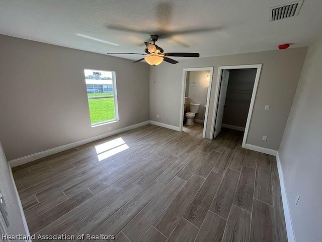 unfurnished bedroom featuring ensuite bath, ceiling fan, dark hardwood / wood-style floors, a walk in closet, and a closet