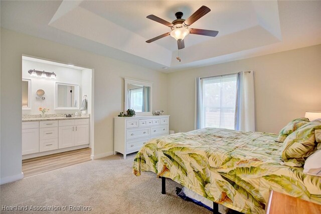 bedroom featuring ceiling fan, multiple windows, connected bathroom, and a tray ceiling