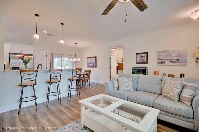 living room with ceiling fan with notable chandelier, light wood-type flooring, and sink