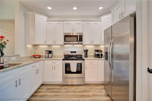 kitchen with light stone countertops, sink, stainless steel appliances, light hardwood / wood-style flooring, and white cabinets