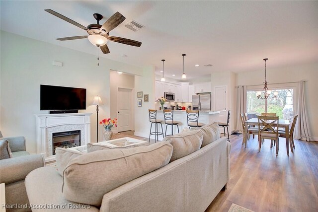 living room with ceiling fan with notable chandelier and light hardwood / wood-style flooring