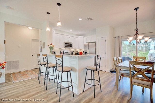 kitchen featuring white cabinetry, a chandelier, decorative light fixtures, appliances with stainless steel finishes, and light wood-type flooring