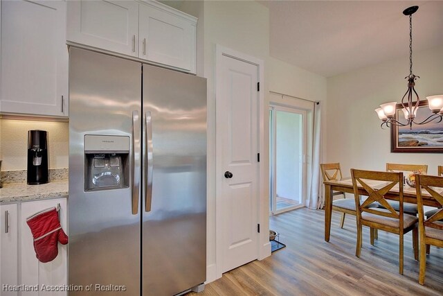 kitchen featuring white cabinets, pendant lighting, light stone counters, and stainless steel refrigerator with ice dispenser