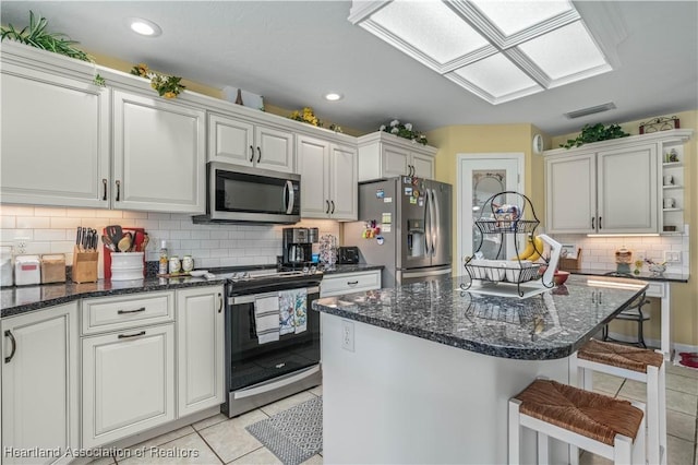 kitchen with stainless steel appliances, light tile patterned floors, white cabinets, a kitchen island, and a breakfast bar area