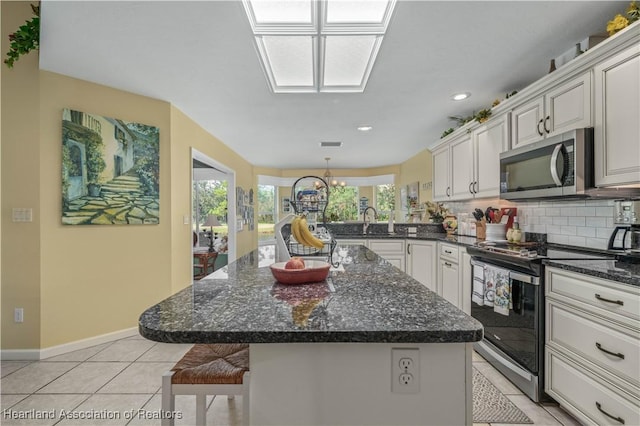 kitchen featuring tasteful backsplash, a kitchen island, light tile patterned floors, and appliances with stainless steel finishes