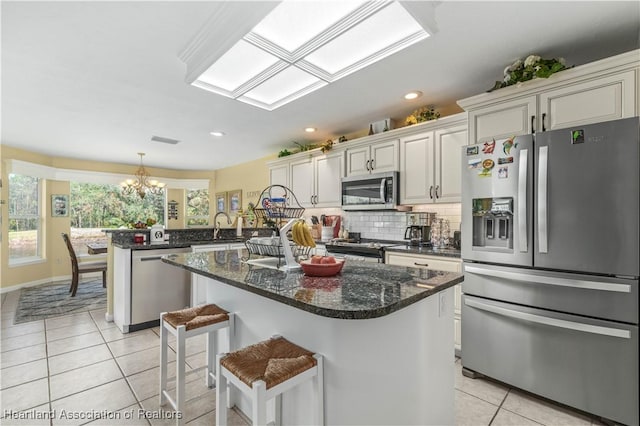 kitchen featuring stainless steel appliances, dark stone countertops, a chandelier, a kitchen island with sink, and light tile patterned flooring